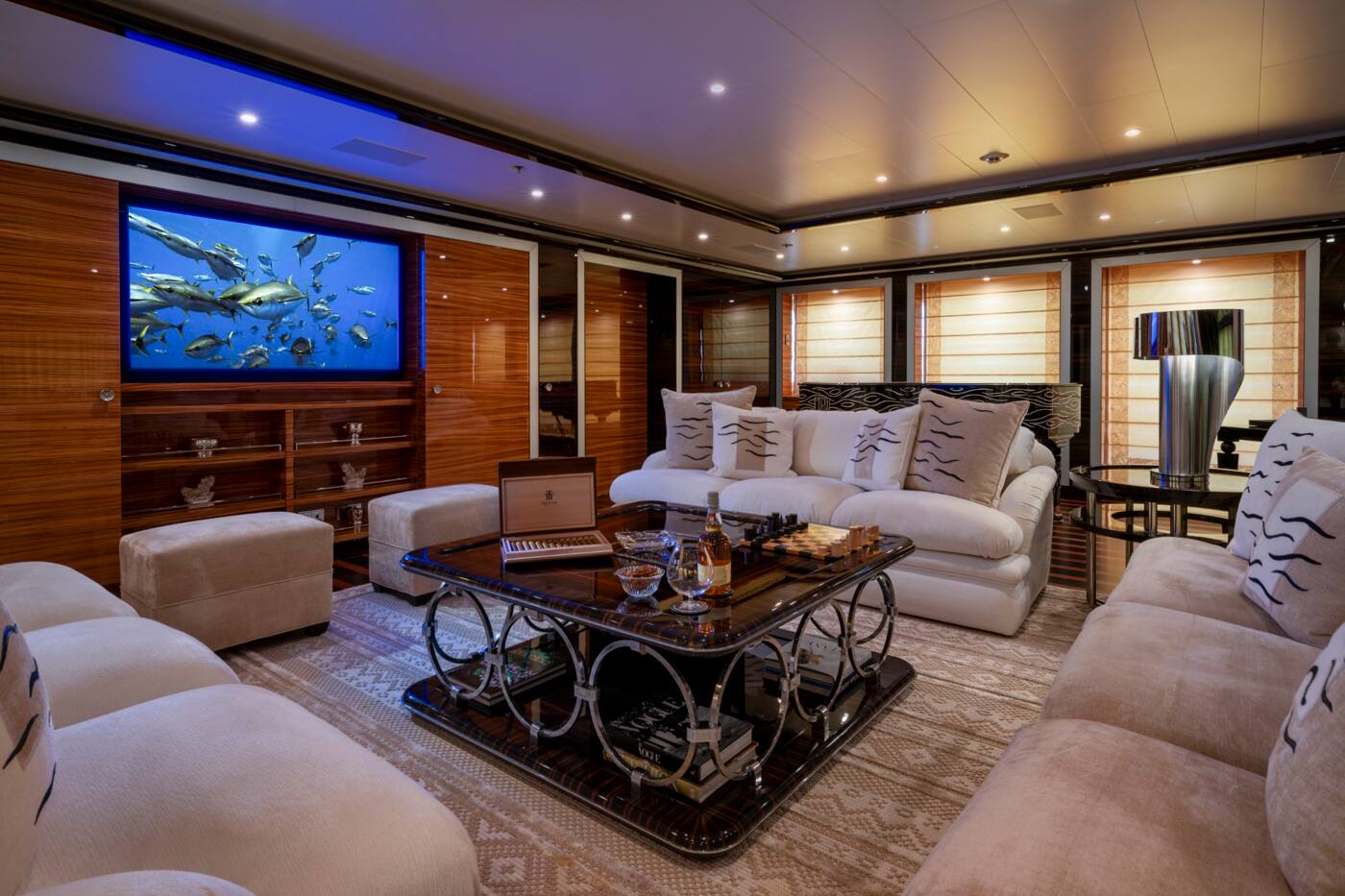 A lounge aboard ALFA NERO with deep cream sofas, a lacquered games table and a large screen