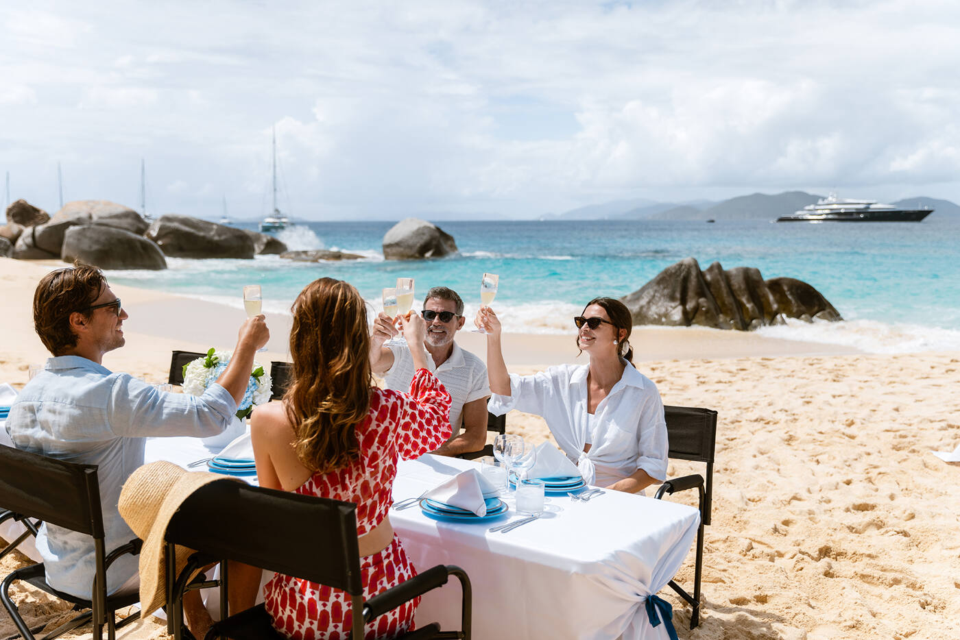 Four guests raising champagne glasses at a table set up on the sand during a CARINTHIA VII charter
